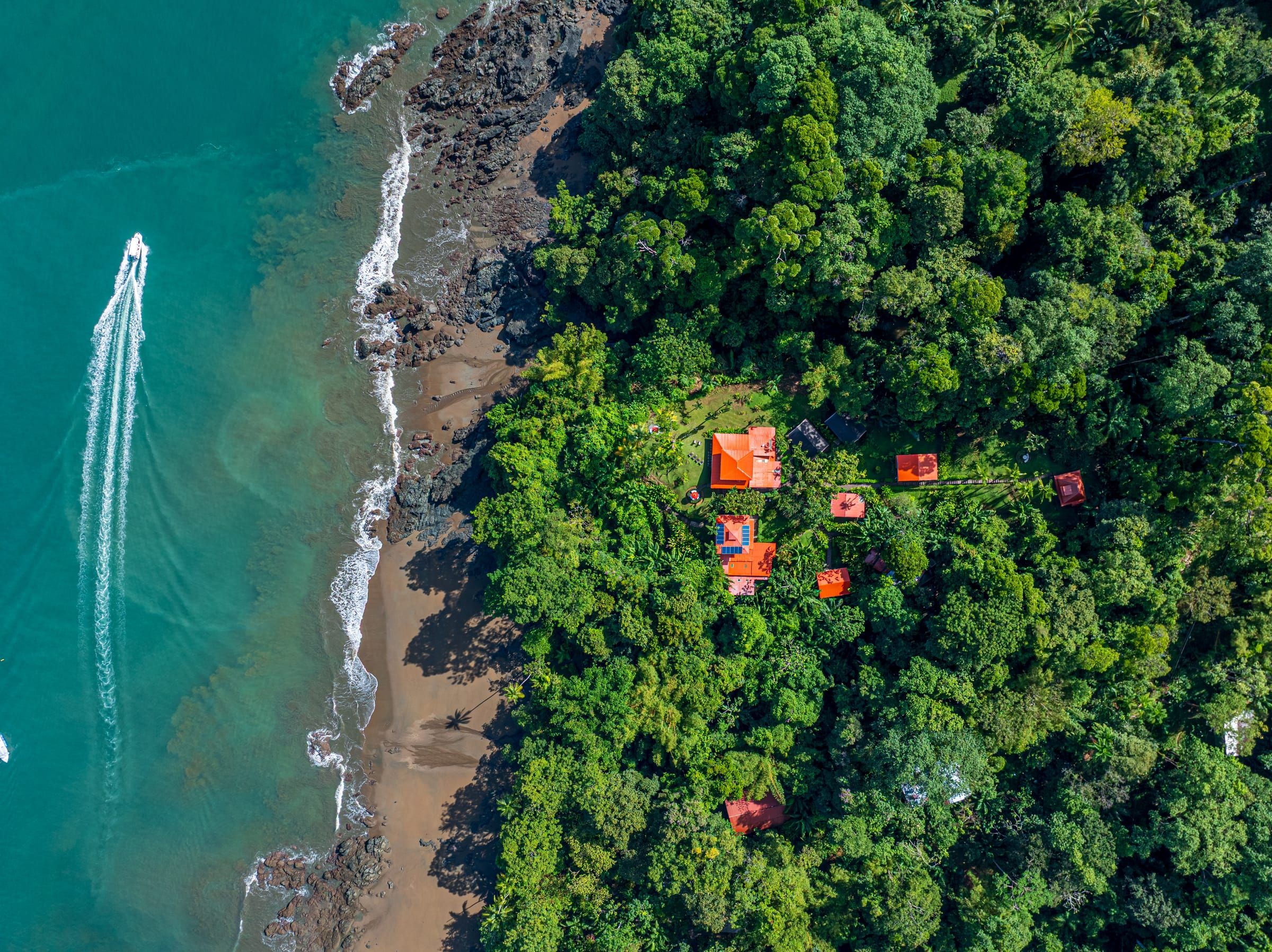 Aerial view of a boat along the coast, with the lodge's red roofs in the forest