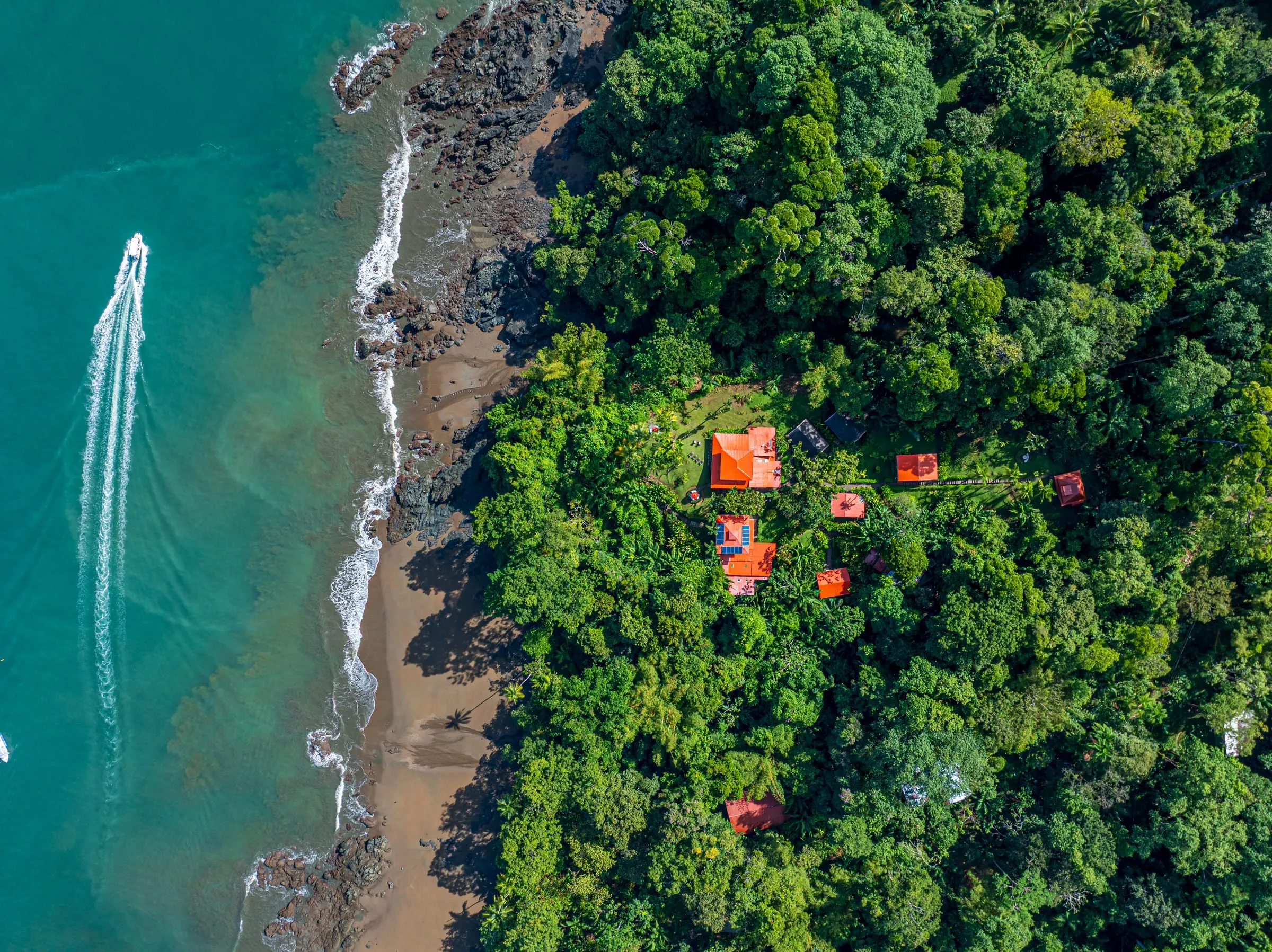 Vista aérea de una lancha junto a la costa, con los techos rojos del lodge en el bosque