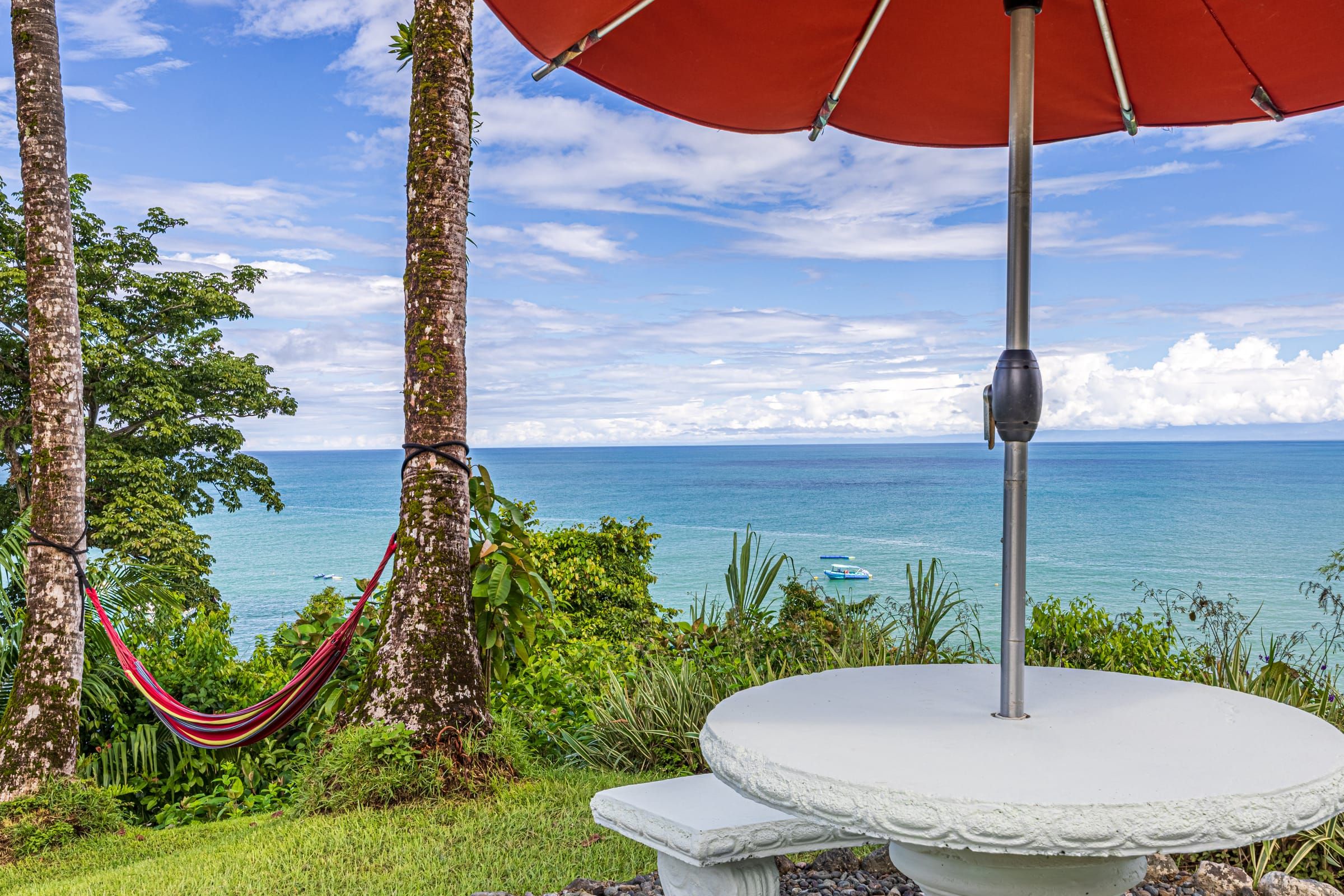 A hammock between palms and a stone table overlooking the ocean