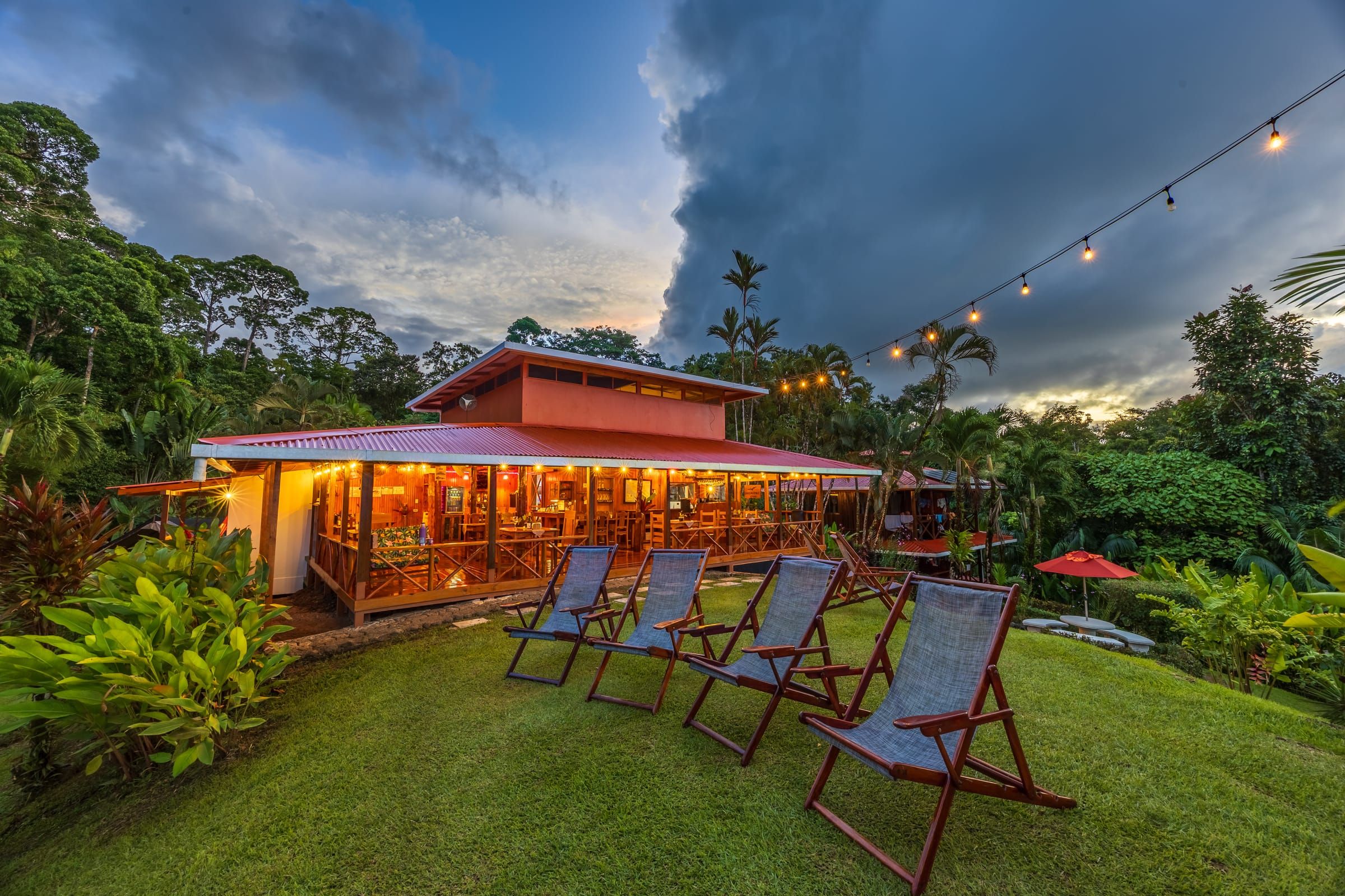 The restaurant lit up at dusk, with deck chairs on the lawn
