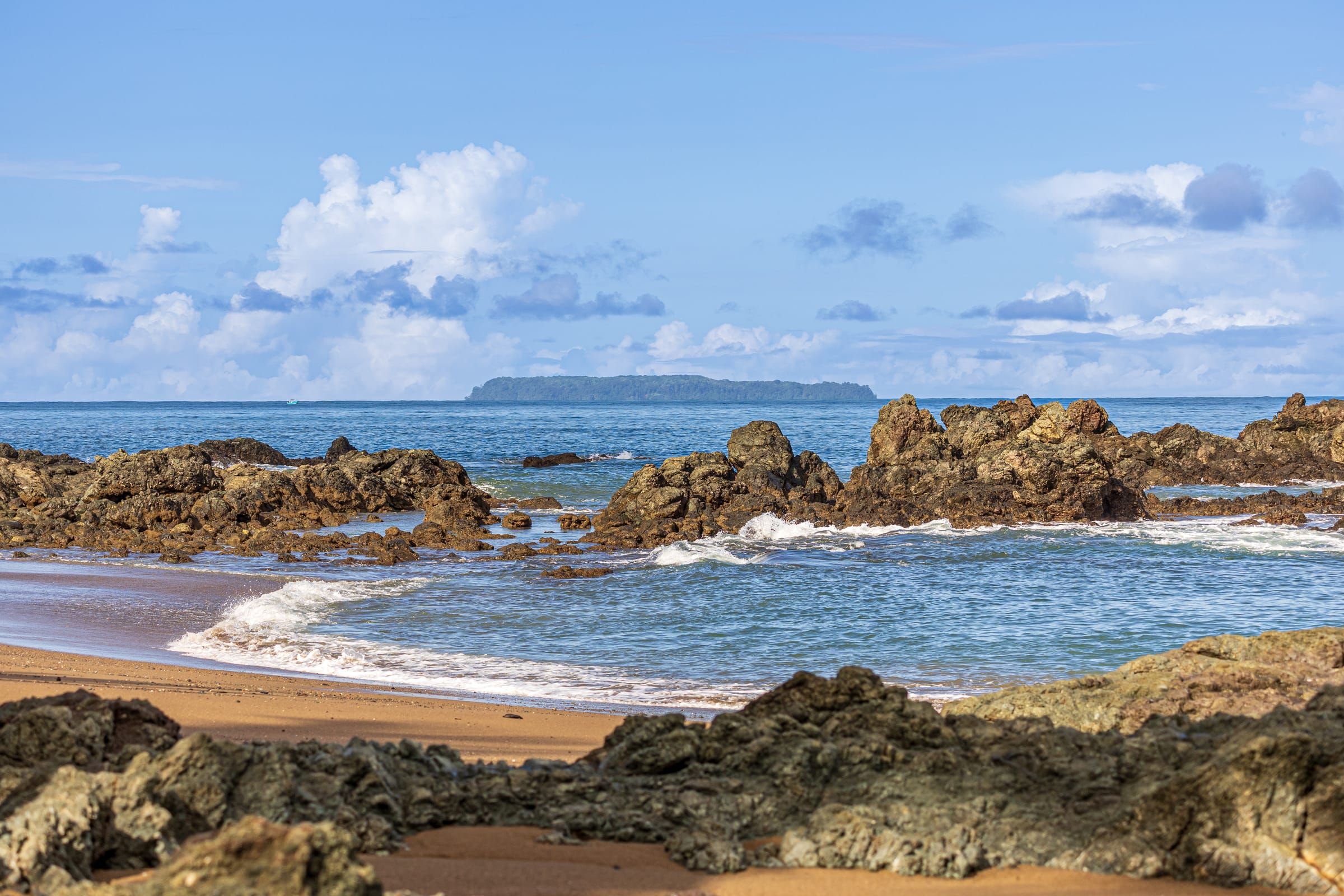 Dark rocks and small waves on the shore, with an island on the horizon